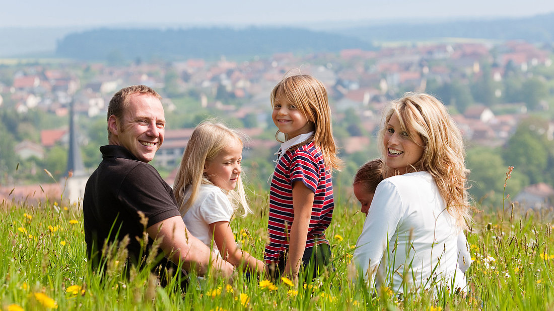Glückliche Familie sitzt auf einer Wiese mit schönem Blick in das Tal.