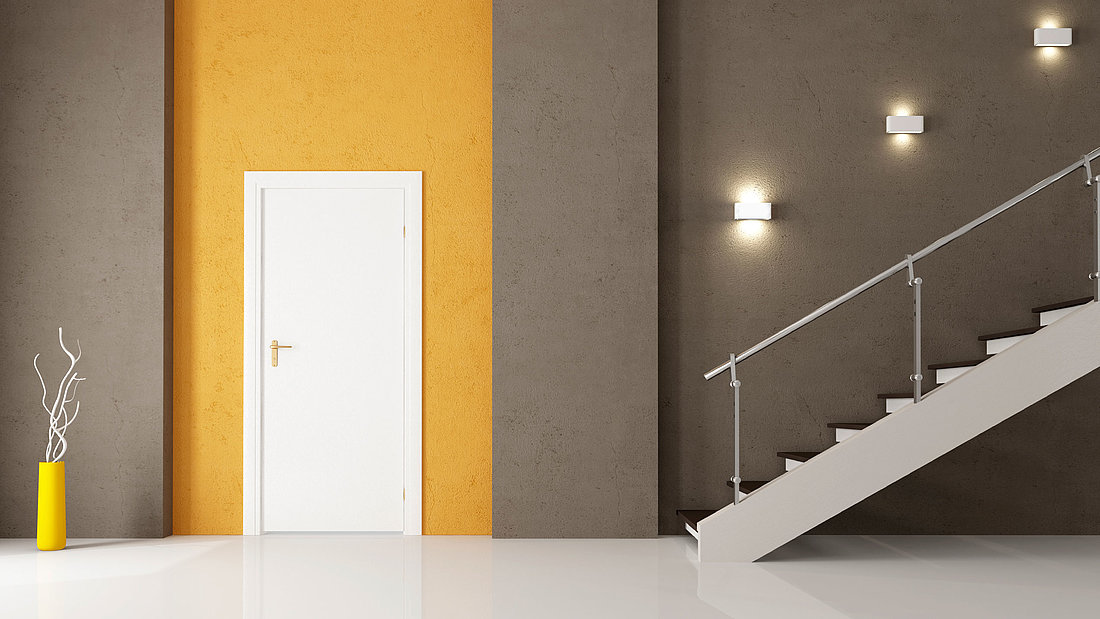 Moderner Flur mit einer Treppe, einer Tür hervorgehoben mit einer gelben Rückwand sowie einer Deko-Pflanze.